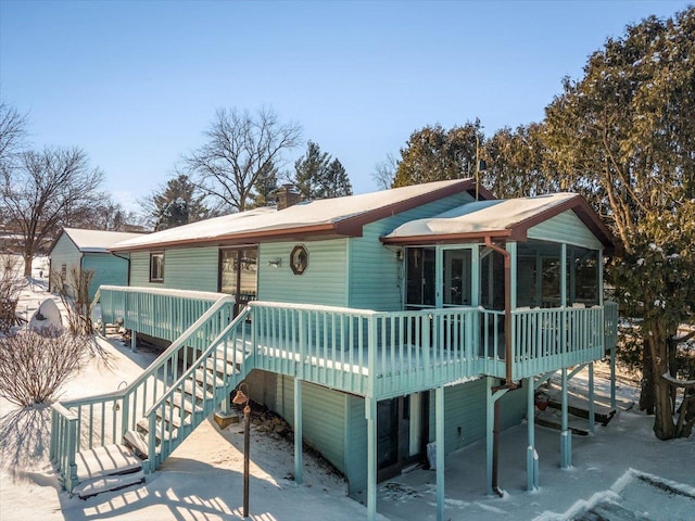 view of front of property with stairs, a chimney, a wooden deck, and a sunroom