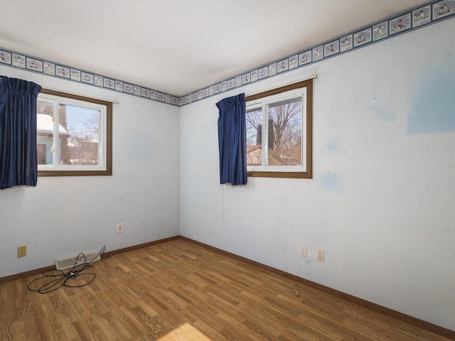 empty room featuring baseboards, visible vents, a wealth of natural light, and wood finished floors