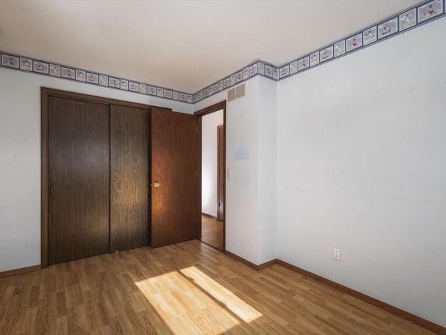 unfurnished bedroom featuring a closet, wood finished floors, visible vents, and baseboards