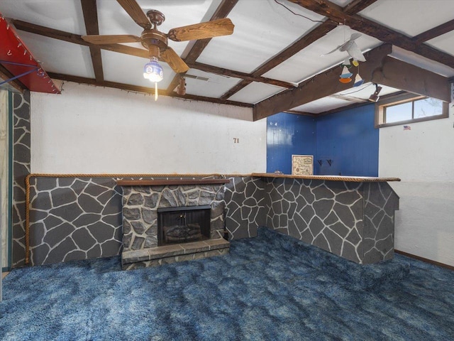 unfurnished living room with ceiling fan, a stone fireplace, beamed ceiling, and carpet flooring