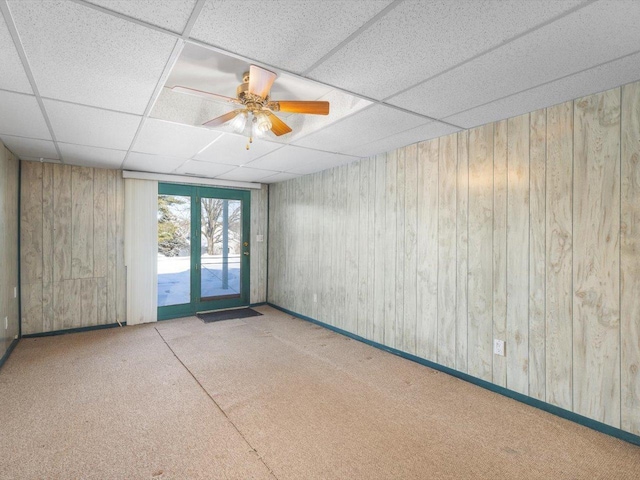 unfurnished room featuring a ceiling fan, a drop ceiling, wood walls, and light carpet