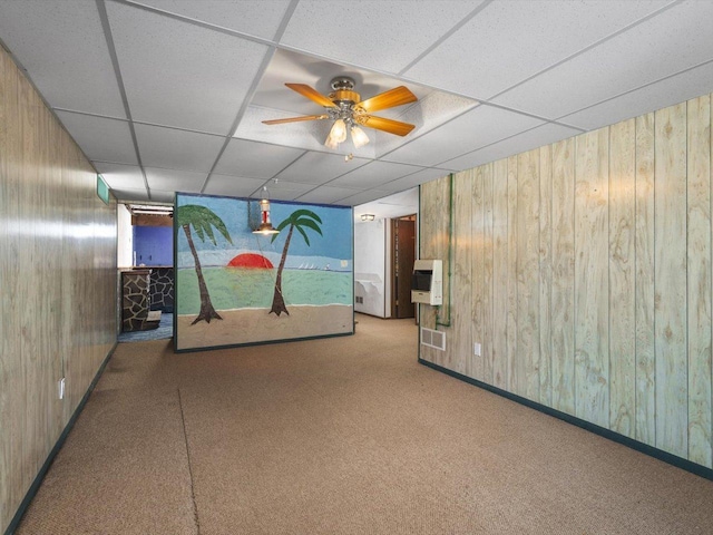 spare room featuring light carpet, wood walls, ceiling fan, and a paneled ceiling