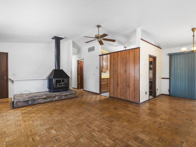 unfurnished living room featuring high vaulted ceiling, a wood stove, visible vents, and ceiling fan with notable chandelier