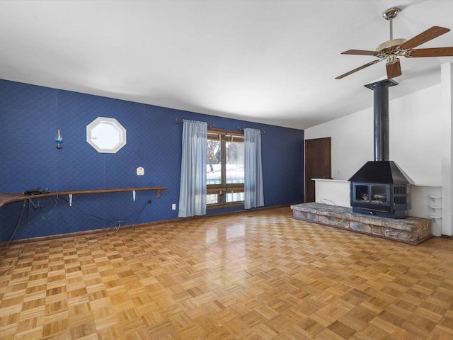 unfurnished living room with a wood stove, vaulted ceiling, and ceiling fan