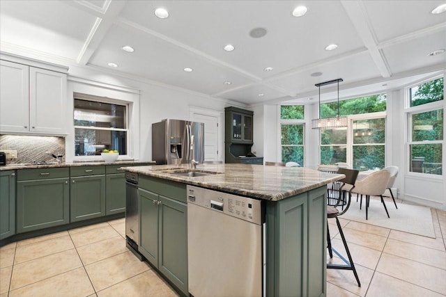 kitchen featuring an island with sink, green cabinetry, hanging light fixtures, stainless steel fridge, and dishwasher