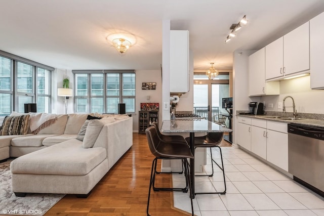 kitchen featuring a breakfast bar, sink, dishwasher, stone counters, and white cabinets