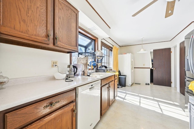 kitchen featuring white appliances, a sink, light countertops, brown cabinetry, and decorative light fixtures