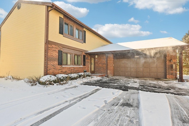 view of snowy exterior featuring brick siding and an attached garage