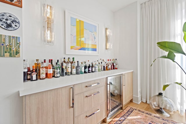 bar with light brown cabinets, wine cooler, and light hardwood / wood-style floors