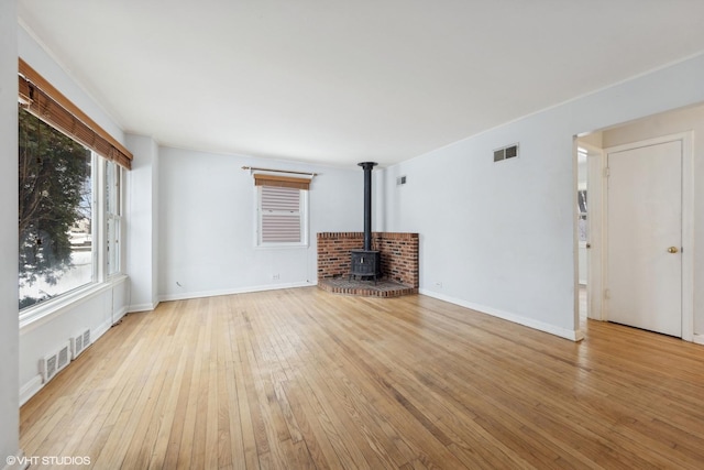 unfurnished living room with light wood-type flooring, a wood stove, visible vents, and baseboards