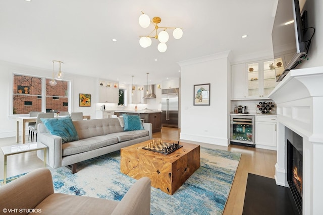 living room featuring an inviting chandelier, light hardwood / wood-style floors, beverage cooler, and indoor bar