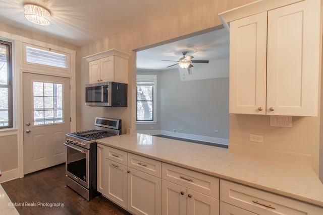 kitchen with appliances with stainless steel finishes, white cabinetry, dark hardwood / wood-style flooring, ceiling fan, and light stone countertops