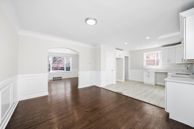 kitchen featuring wood finished floors, arched walkways, a sink, white cabinets, and backsplash