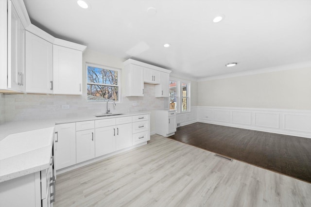 kitchen featuring light wood finished floors, visible vents, light stone counters, wainscoting, and a sink