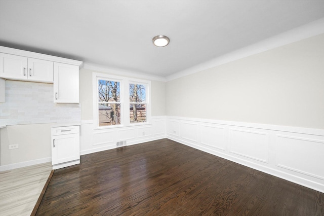 unfurnished dining area with visible vents, wainscoting, and wood finished floors