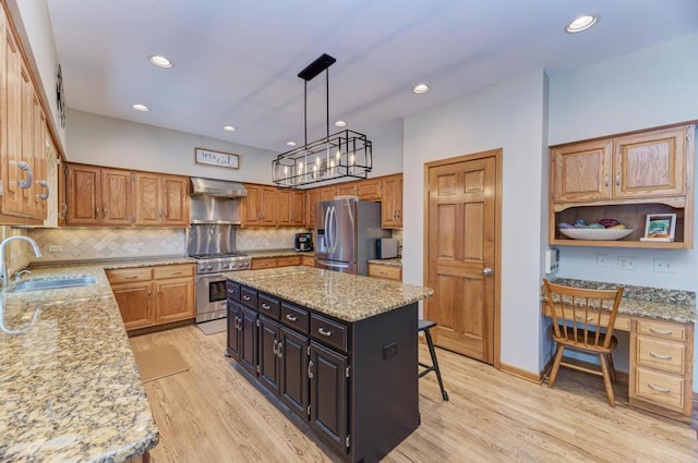 kitchen with a kitchen island, sink, appliances with stainless steel finishes, built in desk, and wall chimney exhaust hood