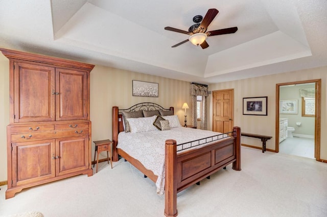 bedroom with light carpet, ceiling fan, a tray ceiling, and connected bathroom