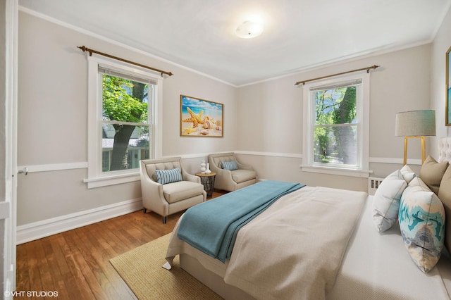 bedroom with crown molding, multiple windows, baseboards, and wood finished floors