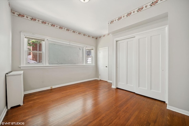 unfurnished bedroom with a closet, multiple windows, baseboards, and wood finished floors