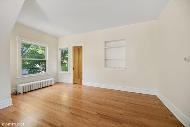 spare room featuring built in shelves, light wood-type flooring, baseboards, and radiator heating unit