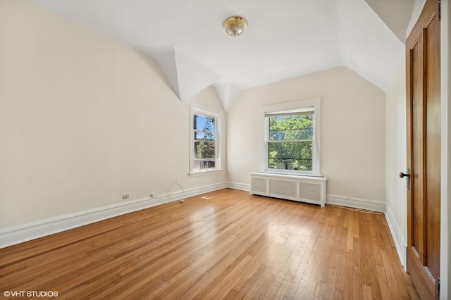 additional living space with radiator, baseboards, vaulted ceiling, and light wood finished floors