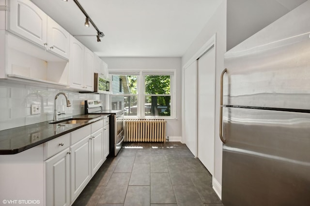 kitchen with appliances with stainless steel finishes, radiator, white cabinetry, and a sink