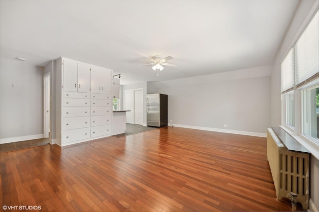 unfurnished living room featuring baseboards, dark wood finished floors, a ceiling fan, and radiator