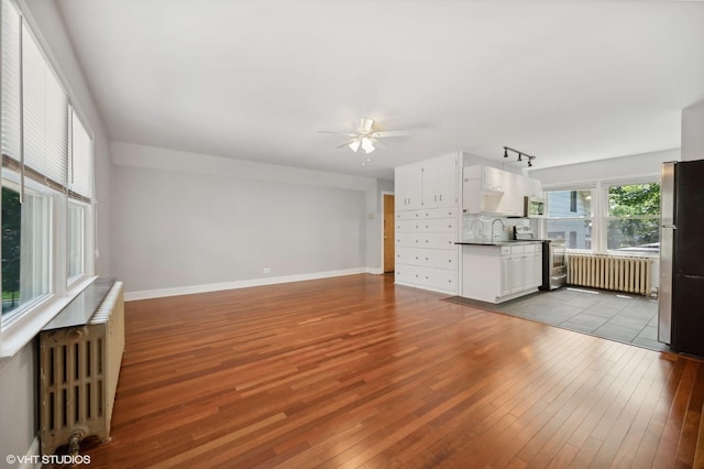 unfurnished living room featuring radiator, baseboards, ceiling fan, and hardwood / wood-style floors