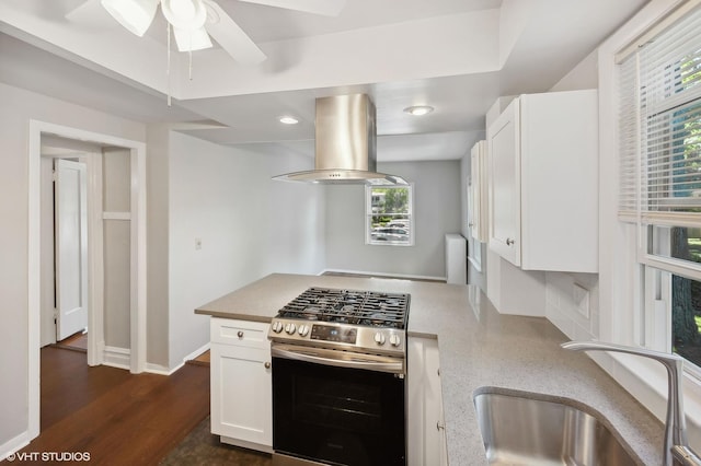 kitchen featuring white cabinets, stainless steel range with gas stovetop, island exhaust hood, and a sink