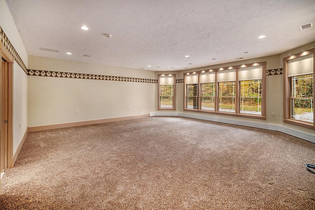 unfurnished room with carpet floors, baseboards, visible vents, and a textured ceiling