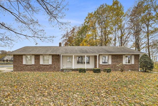 ranch-style house featuring a shingled roof, a chimney, a front lawn, and brick siding