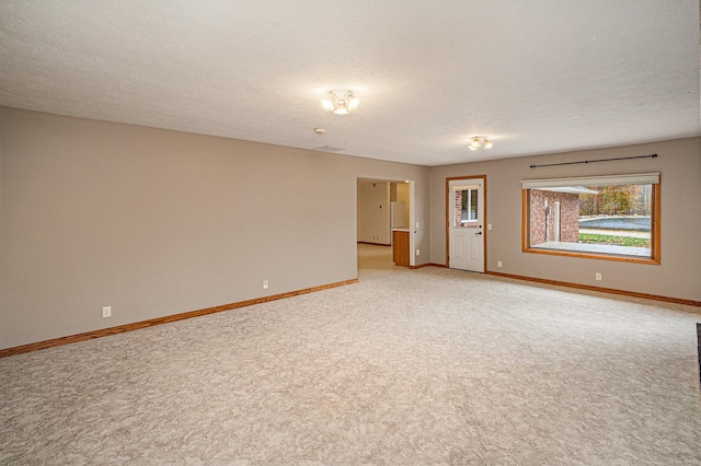 empty room with a textured ceiling, light colored carpet, and baseboards
