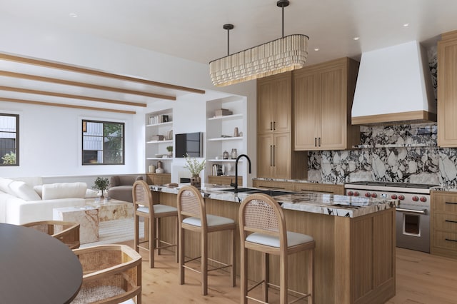 kitchen with stainless steel range, hanging light fixtures, custom range hood, and a center island with sink