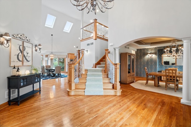 foyer entrance with hardwood / wood-style flooring, a towering ceiling, a notable chandelier, and ornate columns