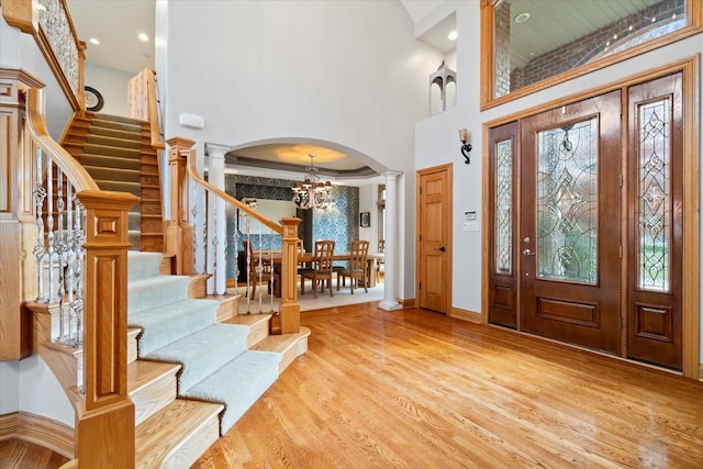 foyer featuring a towering ceiling, a notable chandelier, light hardwood / wood-style flooring, and ornate columns