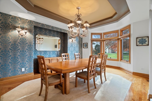 dining area featuring an inviting chandelier, light hardwood / wood-style flooring, and a raised ceiling