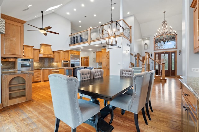 dining space featuring a towering ceiling, ceiling fan with notable chandelier, and light hardwood / wood-style flooring