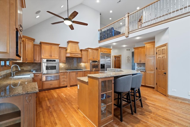 kitchen with premium range hood, sink, a center island, stone counters, and stainless steel appliances