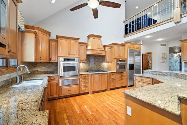 kitchen with sink, light hardwood / wood-style flooring, appliances with stainless steel finishes, custom range hood, and light stone countertops