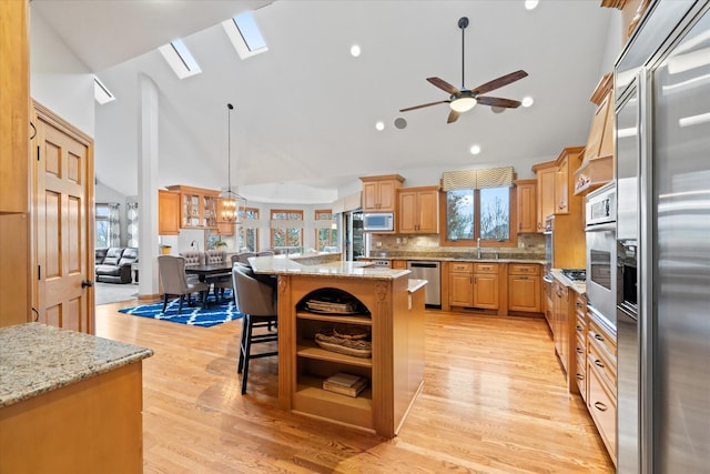 kitchen featuring sink, built in appliances, decorative light fixtures, light stone countertops, and a kitchen island with sink