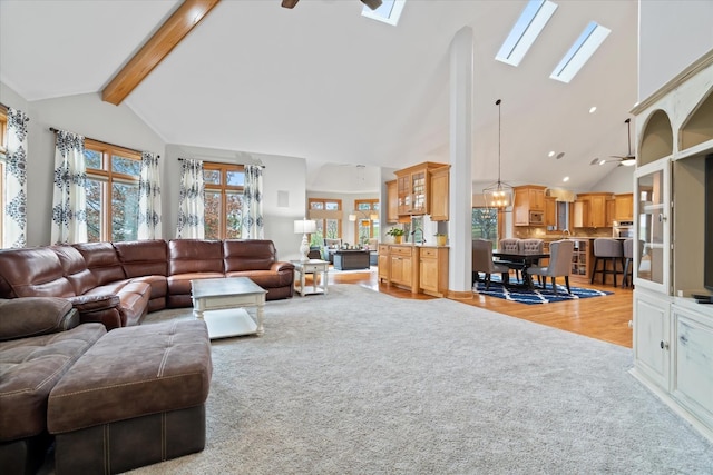 living room featuring beamed ceiling, light wood-type flooring, ceiling fan, and a skylight