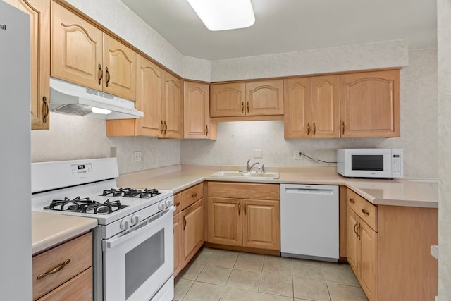 kitchen with under cabinet range hood, white appliances, a sink, light countertops, and light brown cabinetry