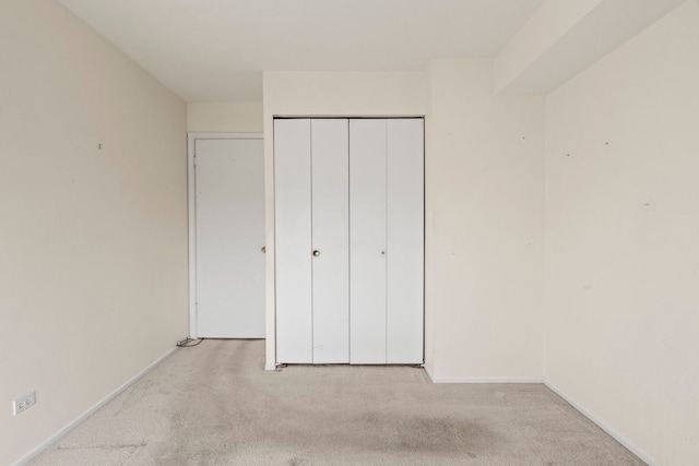 unfurnished bedroom with a closet, light carpet, and baseboards