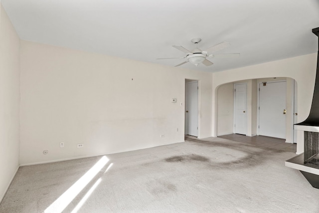 unfurnished living room with arched walkways, carpet, and a ceiling fan