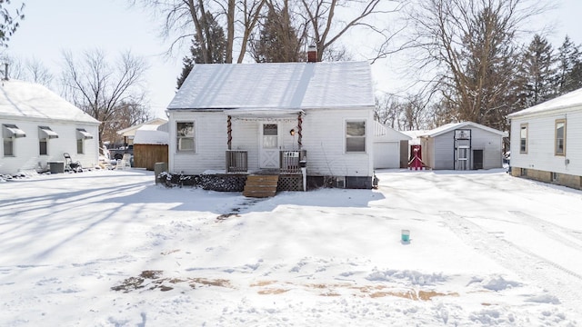 snow covered house featuring a garage and a storage shed