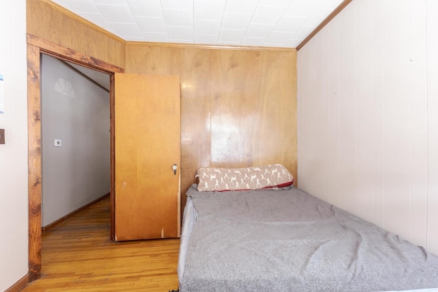 bedroom with ornamental molding, wood walls, and light hardwood / wood-style flooring