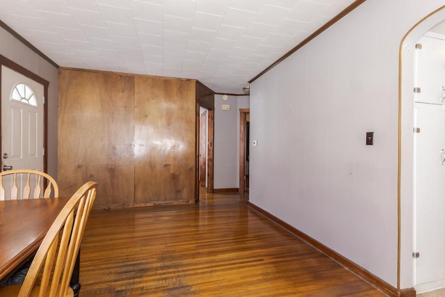unfurnished dining area with dark wood-type flooring, ornamental molding, and wooden walls