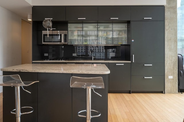 bar with light wood finished floors, stainless steel microwave, a sink, and backsplash