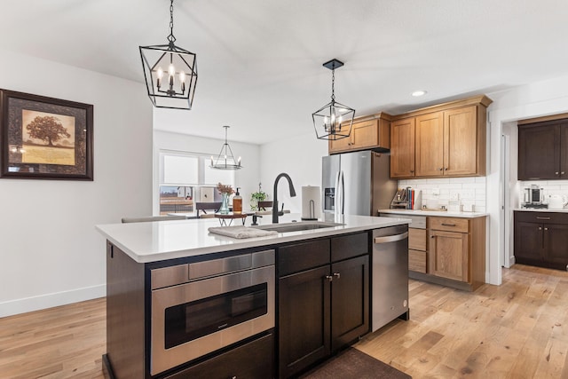 kitchen featuring a sink, a center island with sink, stainless steel appliances, and light countertops