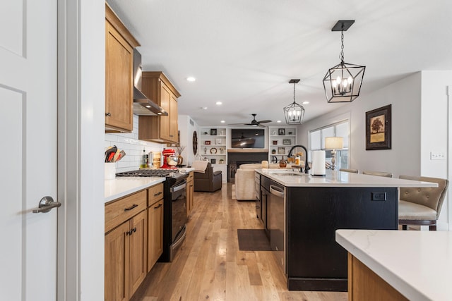 kitchen featuring open floor plan, light countertops, hanging light fixtures, stainless steel gas stove, and an island with sink